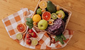 A colorful mix of fruits and vegetables arranged in a basket on a rustic wooden table.