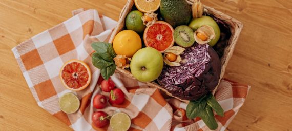 A colorful mix of fruits and vegetables arranged in a basket on a rustic wooden table.